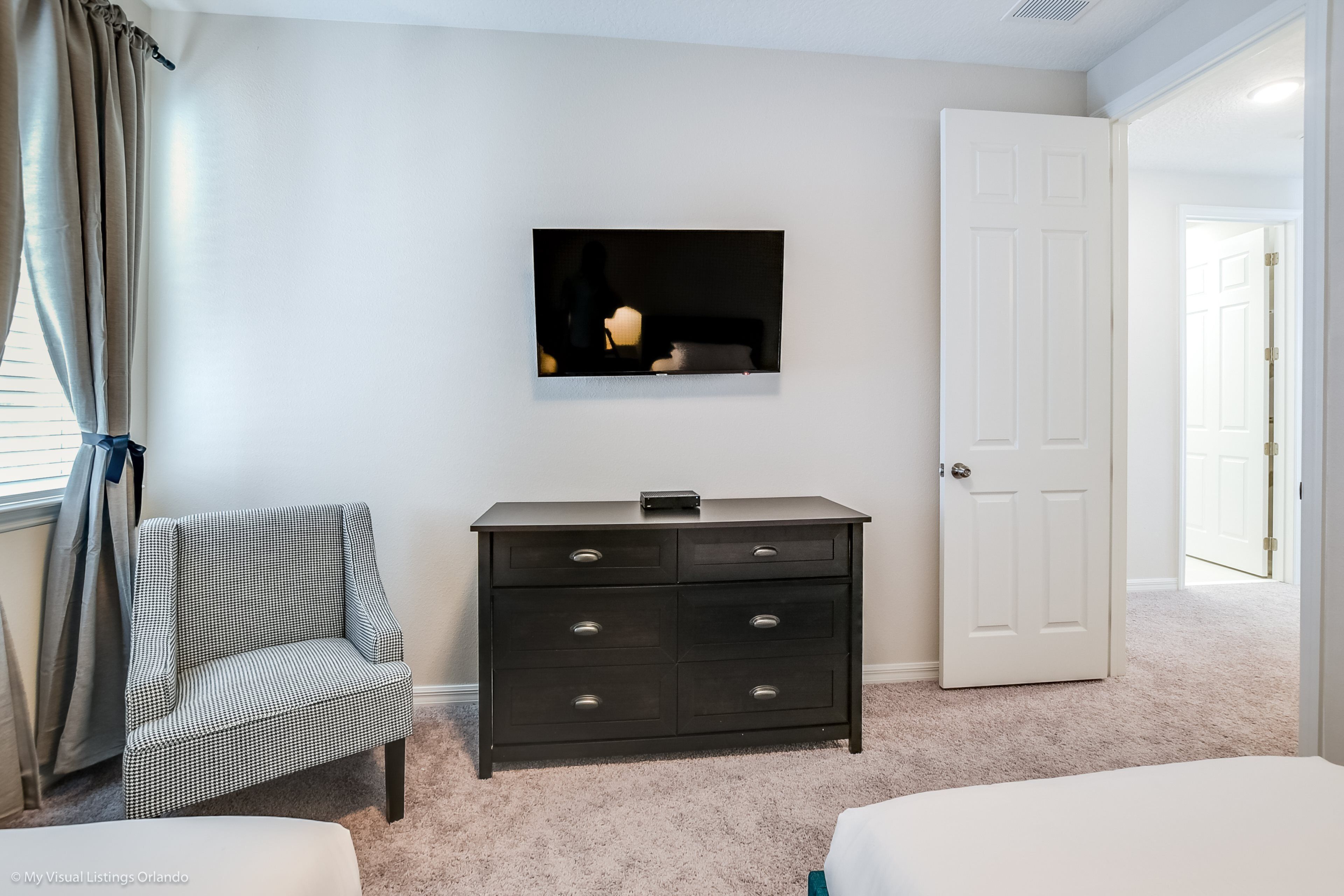 Un dormitorio con cama, cómoda, silla, televisor y puerta.