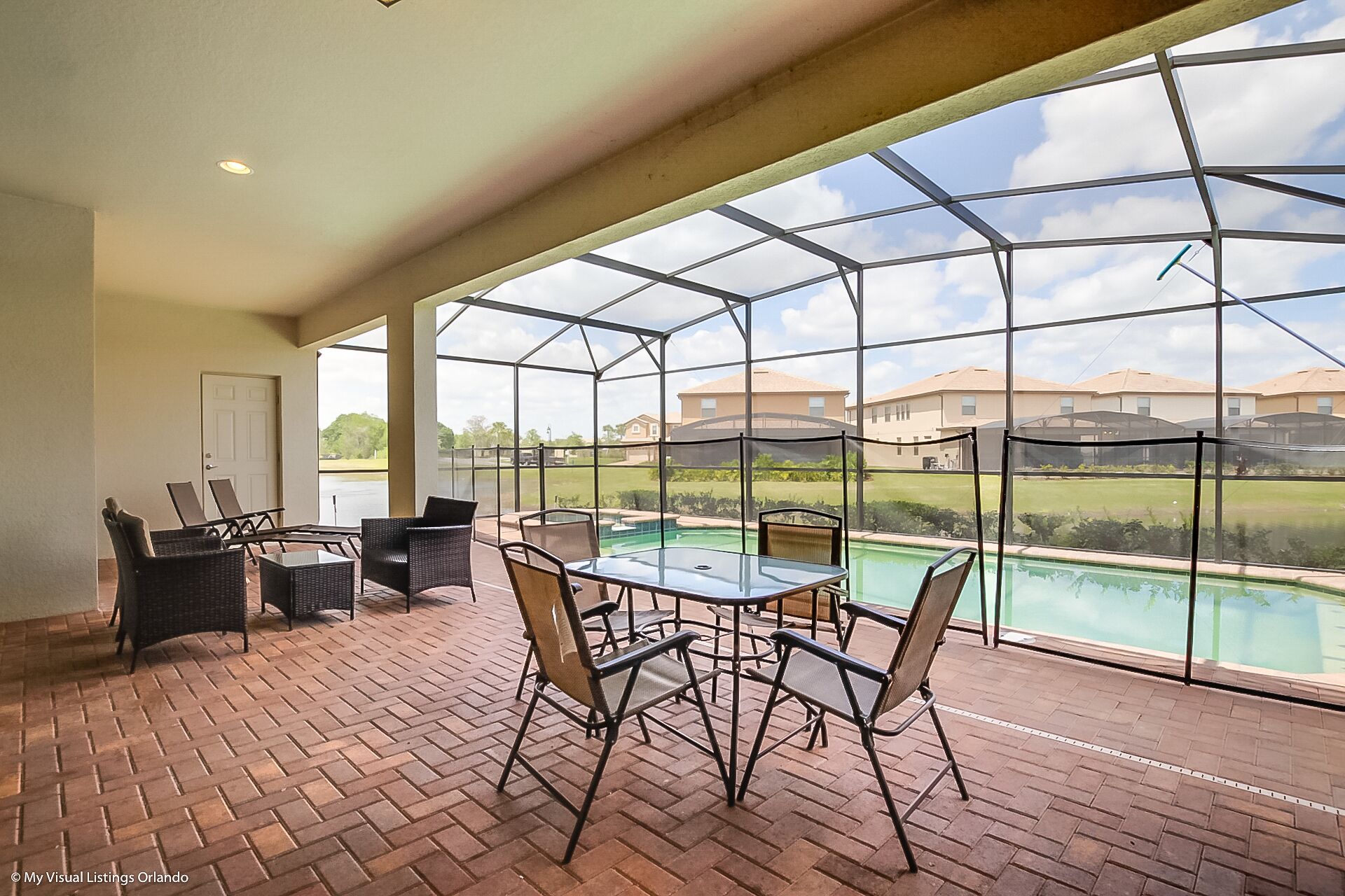 A covered patio with a pool, featuring a glass enclosure, outdoor furniture, and a view of a residential area.