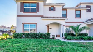 A two-story house with a white exterior, brown trim, and a number '3074' on the front door. There is a well-maintained lawn and a small palm tree in the front yard. - Disney Area 5 Bedroom Private Pool Storey Lake (Kissimmee)