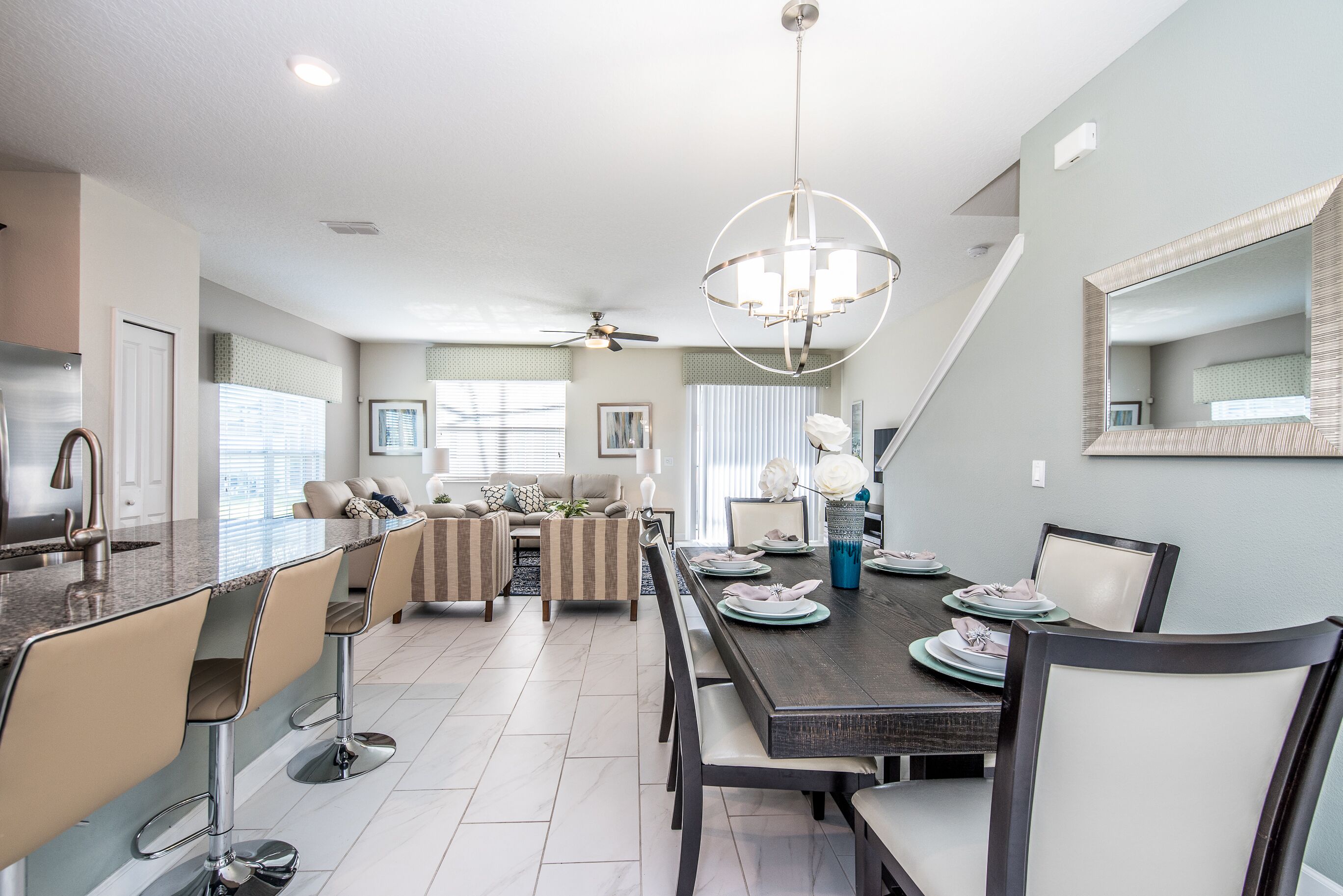 A modern kitchen with a central island, bar stools, a dining table set for six, and a large chandelier.