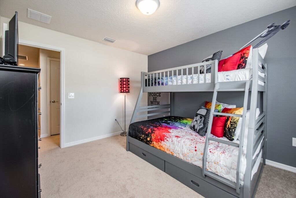 Un lit superposé avec une couvre-lit aux couleurs vives, un bureau avec une chaise et un téléviseur posé sur une commode.