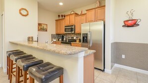 A kitchen with wooden cabinets, a stainless steel refrigerator, a microwave, and a granite countertop. - Paradise Palms IHR 2007 (Kissimmee)
