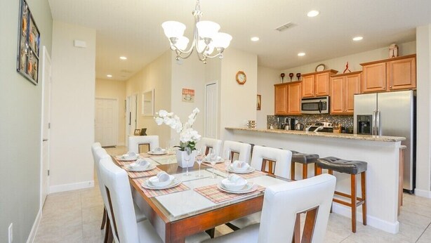 A dining area with a wooden table set for six, white chairs, and a chandelier. - Paradise Palms IHR 2007 (Kissimmee)