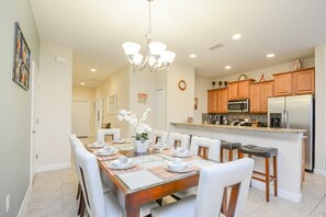 A dining area with a wooden table set for six, white chairs, and a chandelier. - Paradise Palms IHR 2007 (Kissimmee)