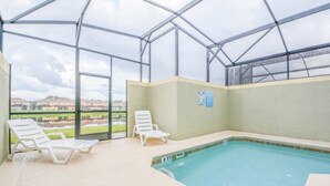 An indoor swimming pool with clear glass walls, two white lounge chairs, and a view of a landscaped area outside. - Paradise Palms IHR 2007 (Kissimmee)