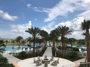 A resort pool area with a central fire pit, lounge chairs, and palm trees.