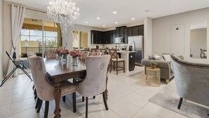 A modern kitchen with dark cabinets, a central island, and a dining area with a chandelier. - Summer Special Solara Villa (Kissimmee)