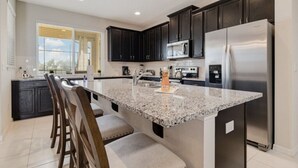 A modern kitchen with dark cabinets, stainless steel appliances, and a granite countertop island with bar stools. - Summer Special Solara Villa (Kissimmee)