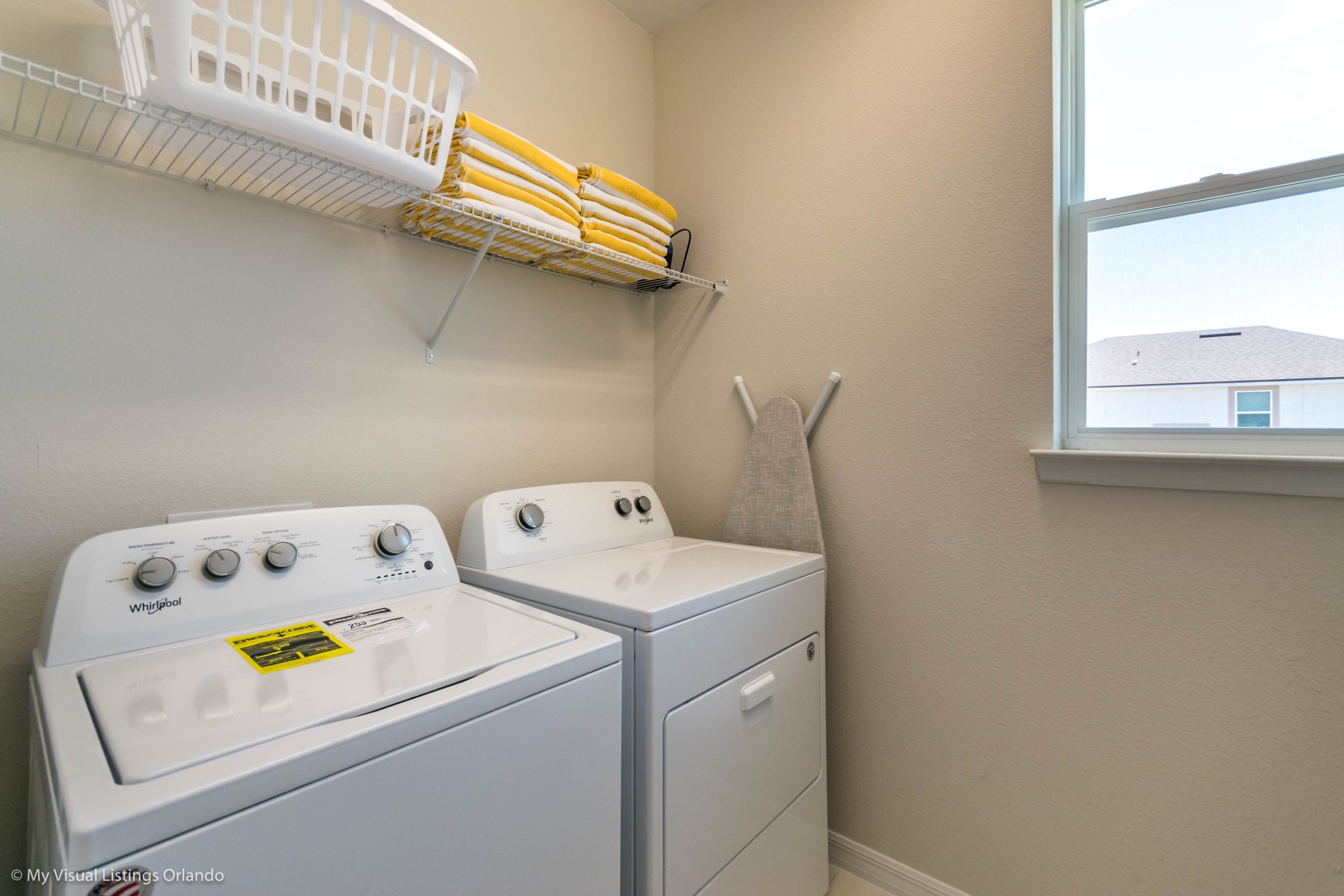 A laundry area with two stacked washers and dryers, a drying rack with towels, and a window with a view of a building outside.