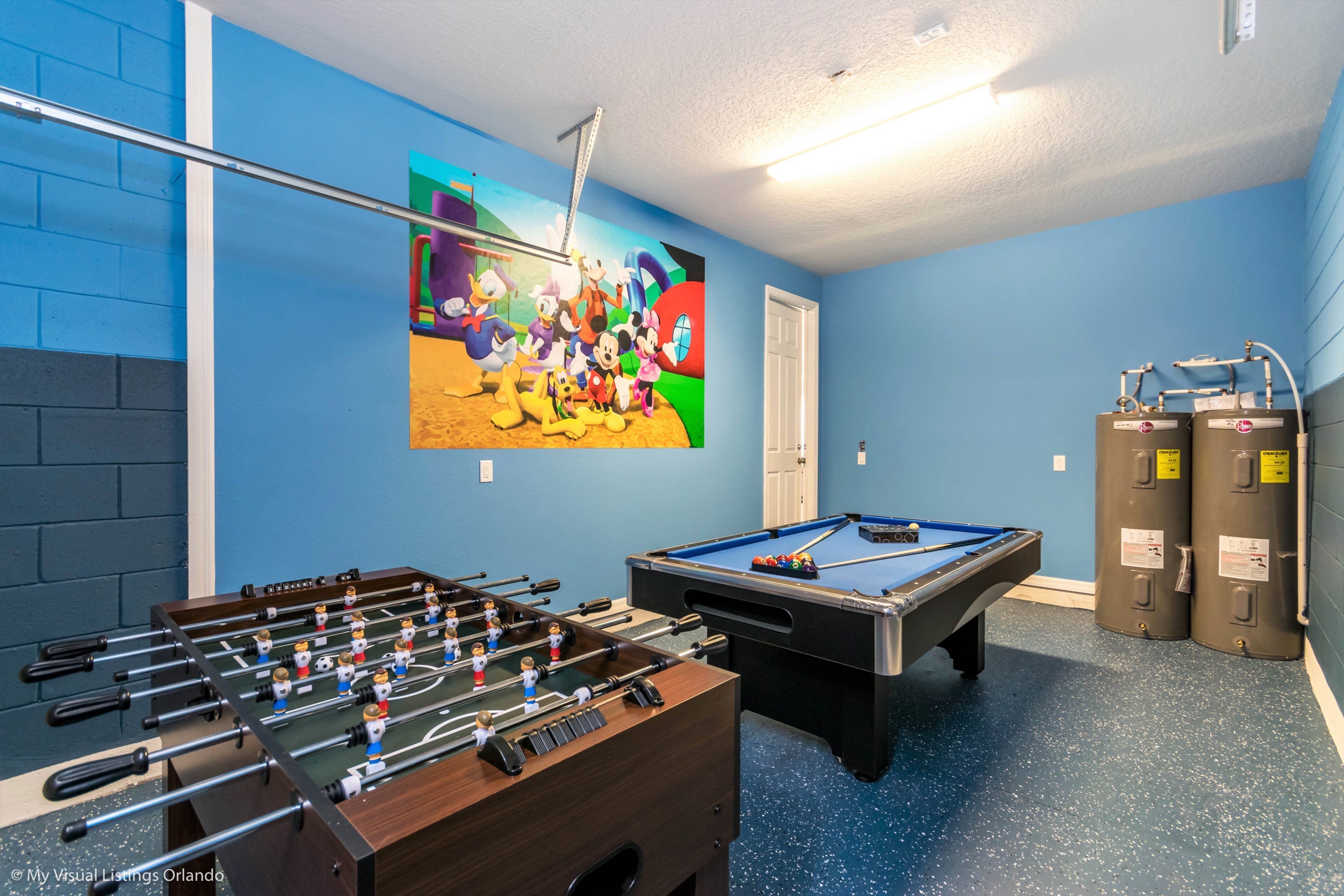 A room with a foosball table, a pool table, and a colorful mural on the wall.
