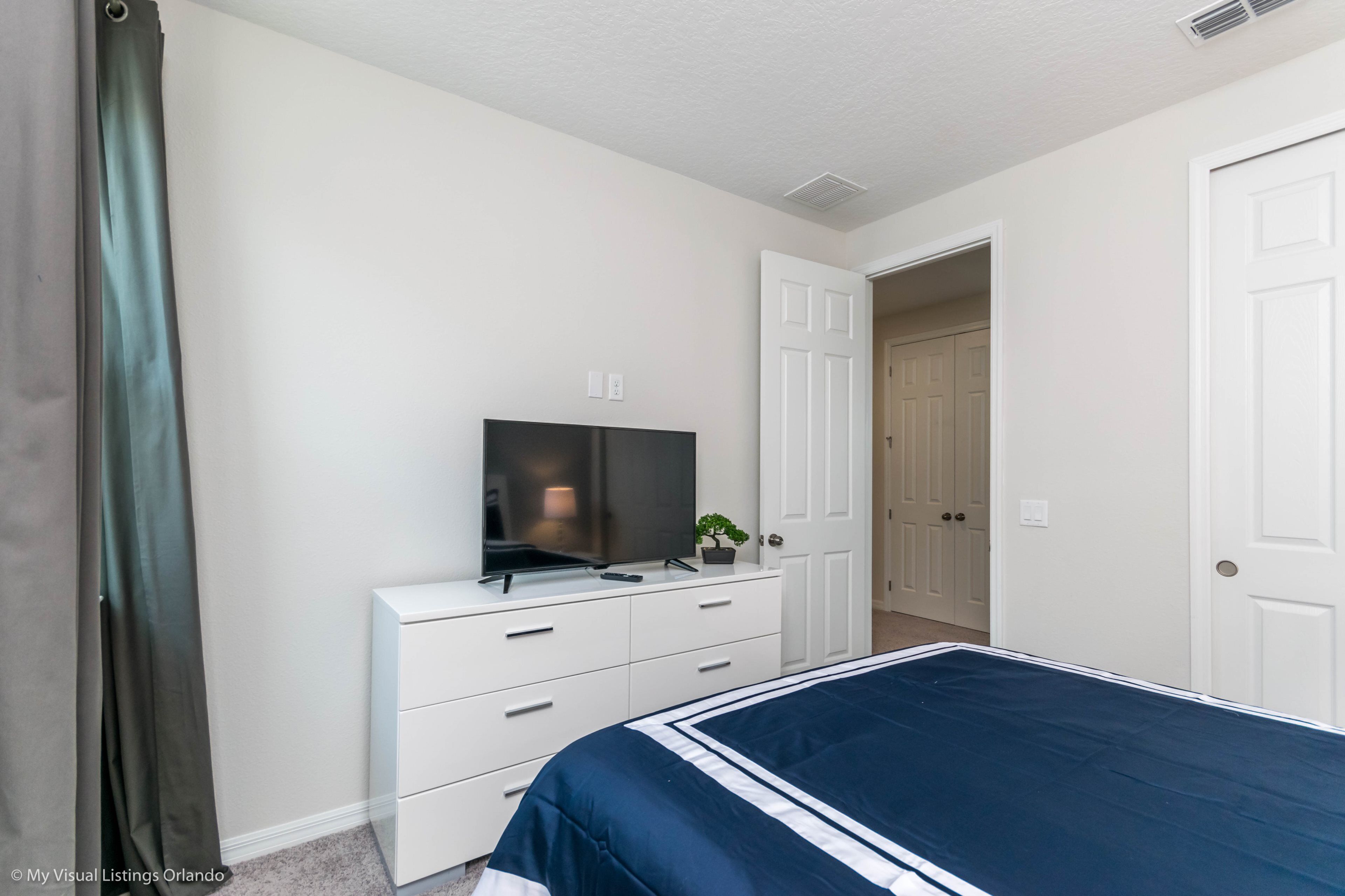 Ein Schlafzimmer mit Bett, Fernseher auf einer Kommode und einer Tür zu einem anderen Raum.