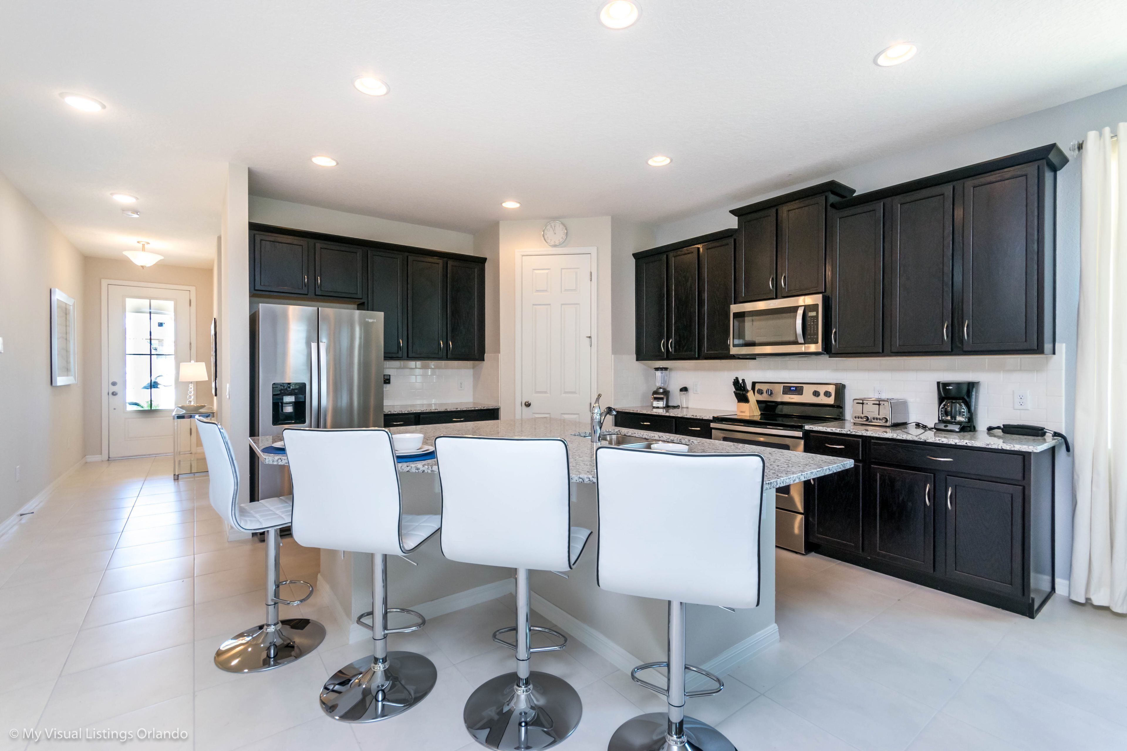 A modern kitchen with dark cabinets, stainless steel appliances, and a central island with bar stools.