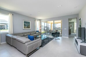 A modern living room with a grey sectional sofa, a glass coffee table, and a flat-screen TV on a white stand. - 7 BD 5 BH With Game Room Pool Spa (Kissimmee)