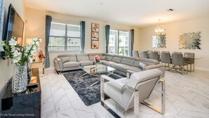 A modern living room with a sectional sofa, a glass coffee table, and a dining area with a chandelier. - 9 Bedroom 5 Bathroom Villa (Davenport)
