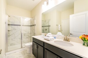 Ein Badezimmer mit Glasdusche, Toilette, Waschbecken mit Spiegel und einer Vase mit Blumen.
