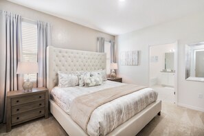 A bedroom with a large bed, two bedside tables, a nightstand, and a door leading to a bathroom.