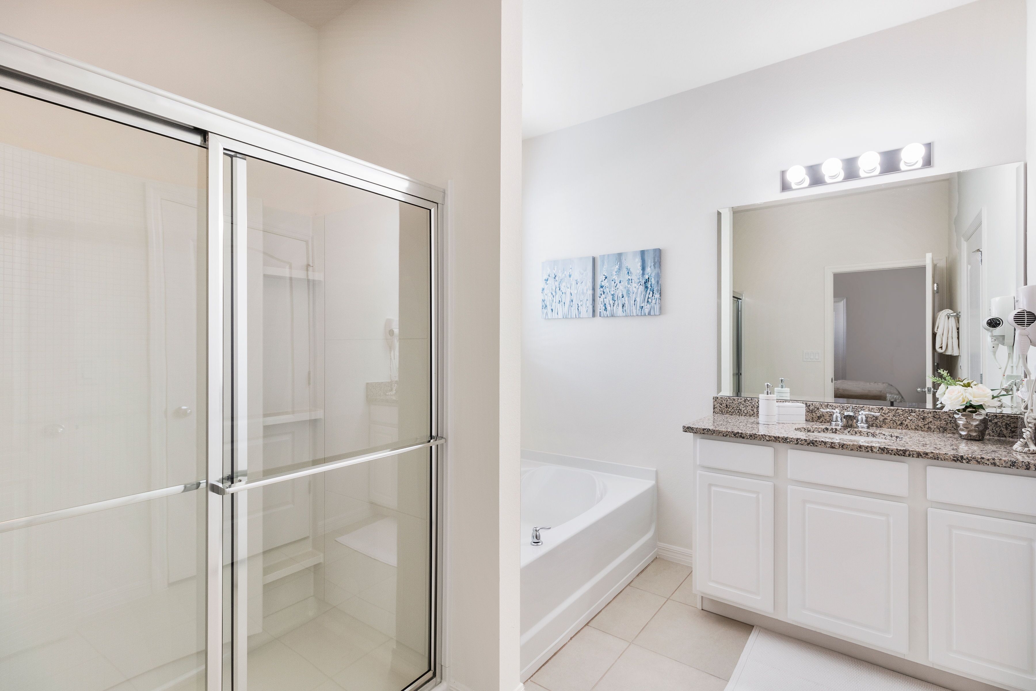 A modern bathroom with a glass shower enclosure, a freestanding bathtub, and a vanity with a large mirror and lights.