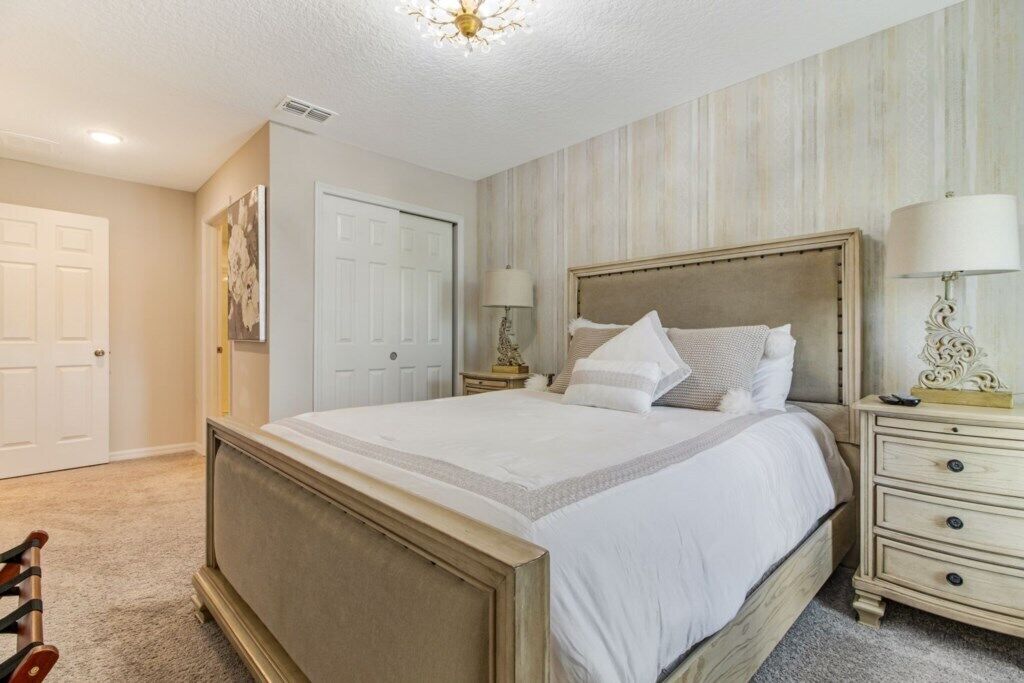 A bedroom with a large bed, two bedside tables, a chandelier, and a door.