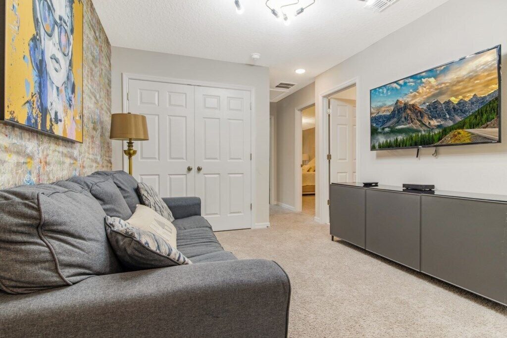 A modern living room with a grey sofa, a flat-screen TV mounted on the wall, and a large painting above the sofa.