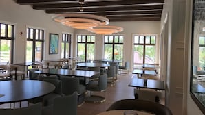 A modern dining area with round tables and chairs, large windows, and a ceiling with circular light fixtures.