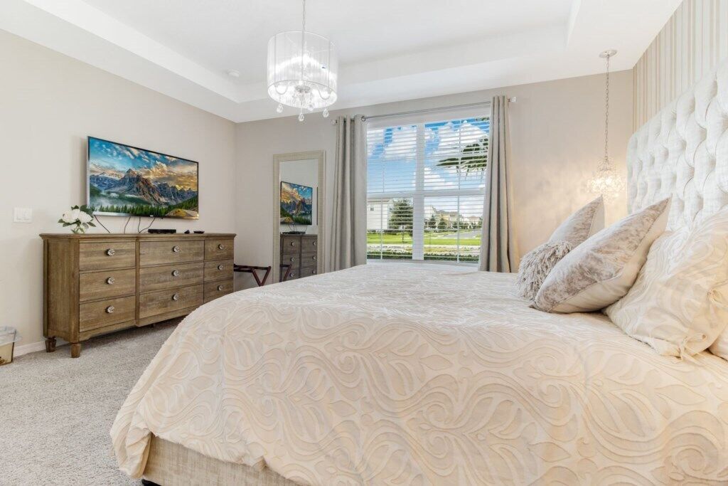 A bedroom with a large bed, a dresser, a chandelier, and a painting on the wall.