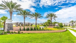 A well-maintained lawn with a sign reading "SOLARA" surrounded by palm trees and a clear blue sky.
