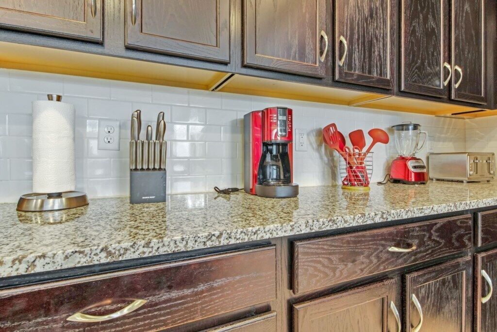 A kitchen with granite countertops, wooden cabinets, a coffee maker, a toaster, and various utensils.