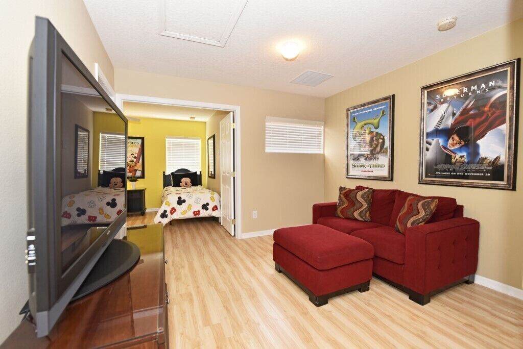 A living room with a red sectional sofa, a flat-screen TV, and two posters on the wall.