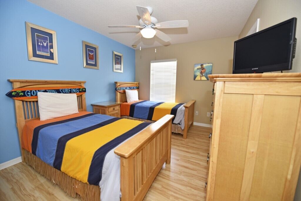 A bedroom with two wooden beds, a ceiling fan, a television, and framed pictures on the wall.