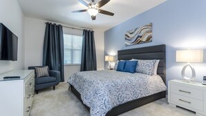 Ein Schlafzimmer mit Bett, Schreibtisch, Stuhl, Deckenventilator und einem Fenster mit Vorhängen.