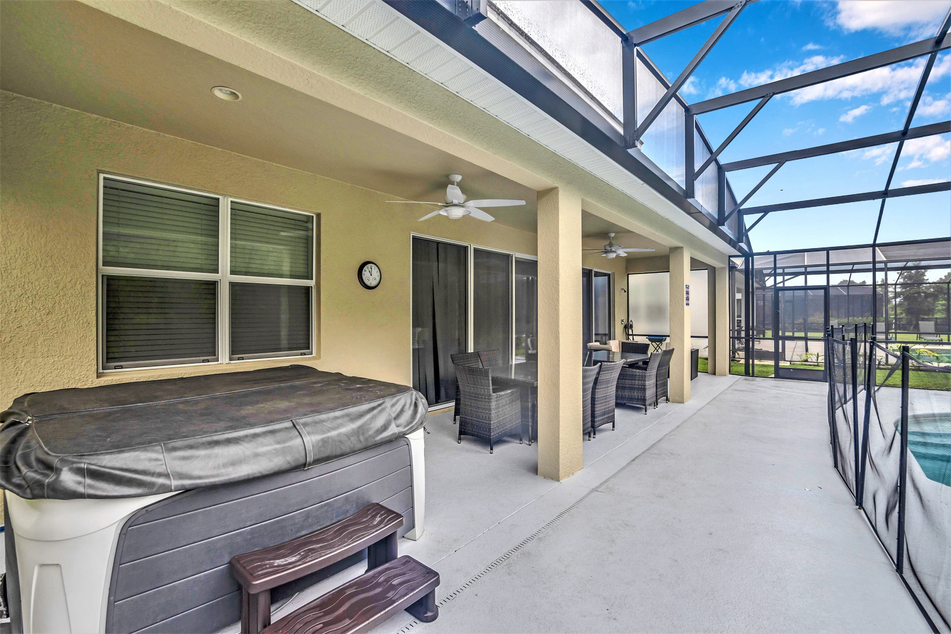 A covered patio area with a hot tub, seating, and a view of a swimming pool.