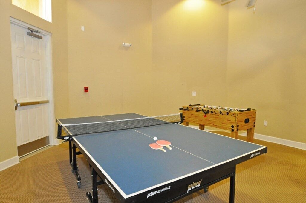 Ett bordtennisbord med boll och racketar, ett fotbollsspel och en vit dörr.