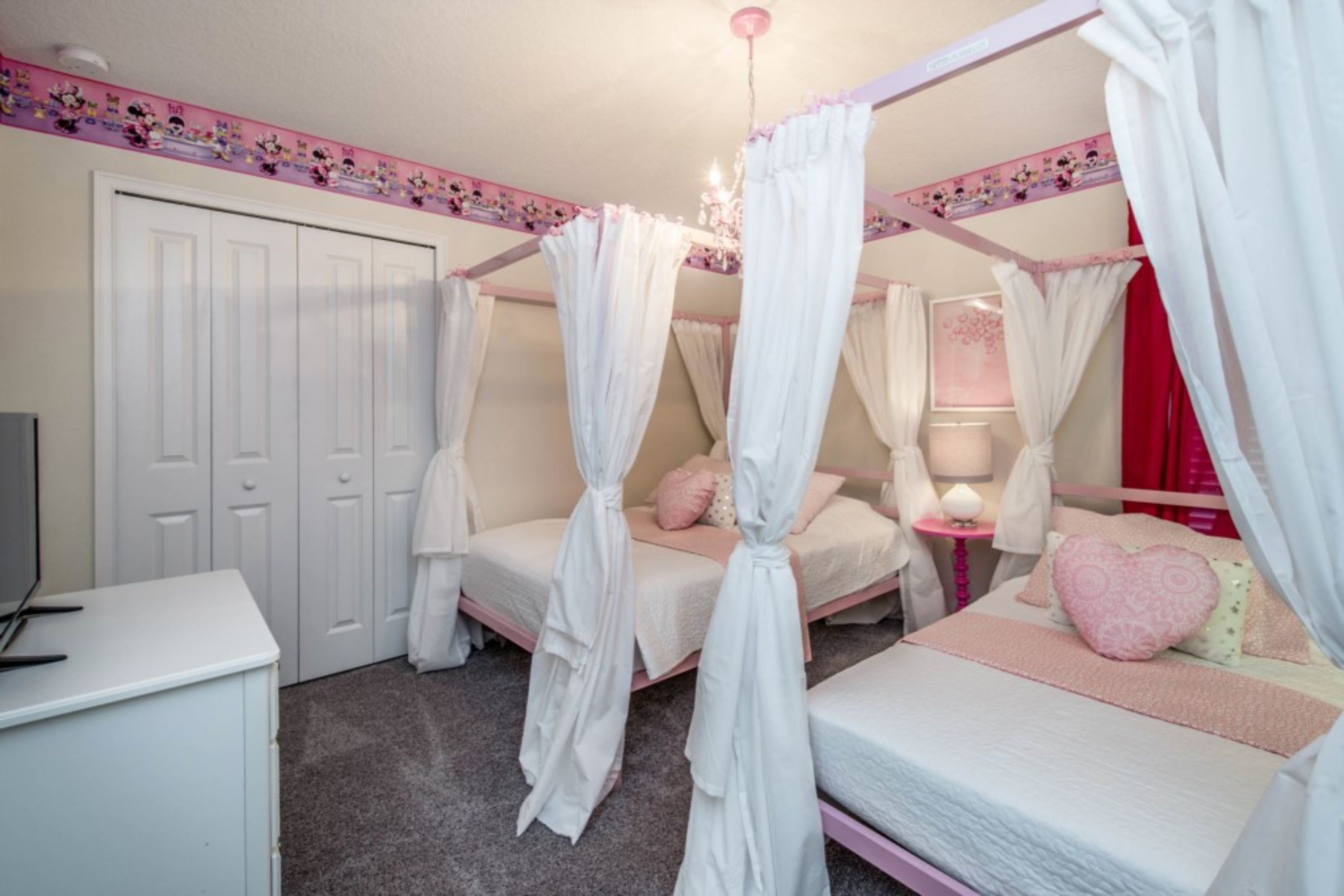A bedroom with a canopy bed, a bedside table with a lamp, and a dresser.