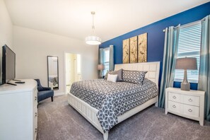 Um quarto com cama, cômoda, televisão e mesa de cabeceira.