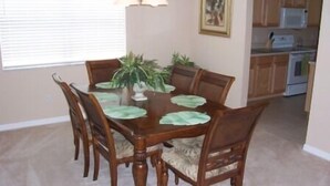 A dining room with a wooden table and chairs, a potted plant, and a kitchen in the background. - 506 Bonville (Davenport)