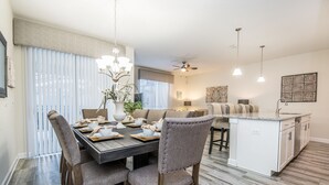 Una cocina moderna con una isla central, una zona de comedor con una mesa de madera oscura y sillas a juego, y un ventilador de techo.