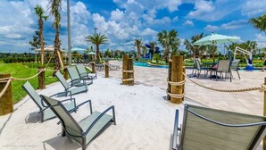 Zona de piscina con sillas de descanso, palmeras y cielo despejado.