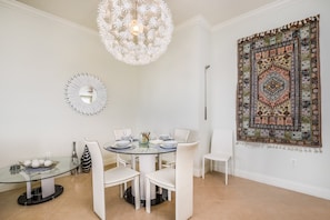 A dining area with a round glass table, white chairs, a decorative mirror, and a hanging light fixture. - Golf View 3 Bedroom Condo (Kissimmee)