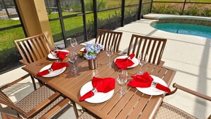 A dining table set for four with red napkins, white plates, and wine glasses, overlooking a swimming pool. - Solterra Resort IHR 3049 (Davenport)