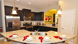 A modern kitchen with dark cabinets, stainless steel appliances, a granite countertop, and a central island with a sink and dining setup. - Solterra Resort IHR 3049 (Davenport)