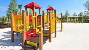 Une aire de jeux avec une structure d’escalade, des toboggans et une maison de jeux au toit rouge.