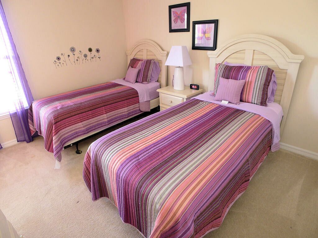 A bedroom with two beds, each with a striped bedspread, a bedside table with a lamp, and a clock.