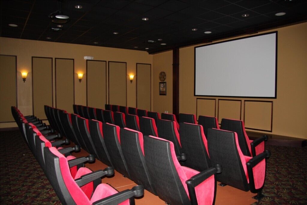 A theater with rows of black and red seats, a large screen, and wall sconces.