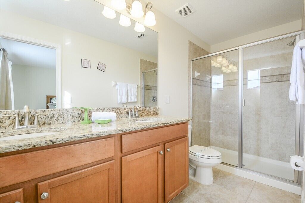 A bathroom with a marble countertop, wooden cabinets, a white toilet, and a glass-enclosed shower.