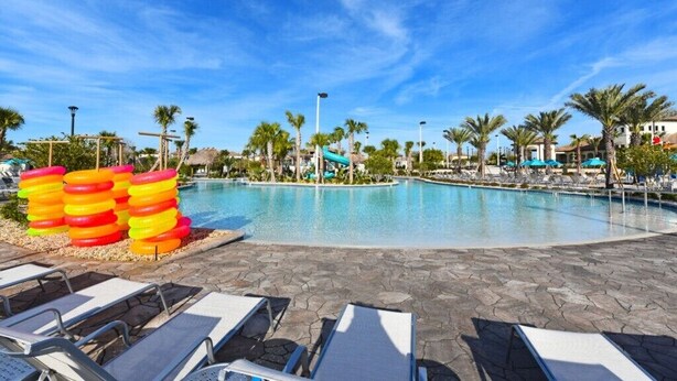 A pool area with lounge chairs, palm trees, and a water slide.