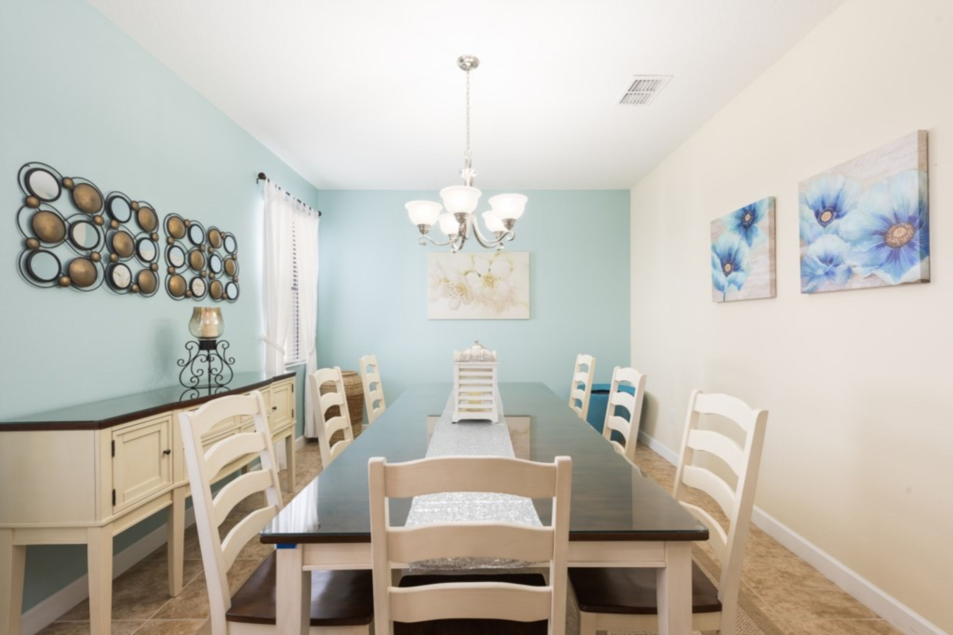 A dining room with a long table, white chairs, a chandelier, and wall art.