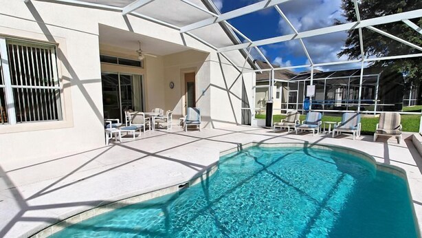 Piscina com água cristalina, cercada por um espaço coberto com espreguiçadeiras e um edifício com grandes janelas.
