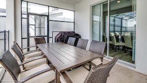 Een eetruimte met een houten tafel en rieten stoelen, grote ramen en een schuifdeur naar een balkon.