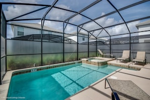 Una piscina con cerramiento de vidrio, sillas de descanso y un jacuzzi.