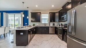 Une cuisine moderne avec des meubles de couleur sombre, des appareils électroménagers en acier inoxydable et un sol en marbre.